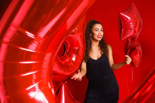 Funny girl with red balloons on a red background. Young woman festive mood with balloons in the form of numbers and stars.