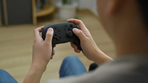 View over shoulder of young man holding wireless controller playing video game. Entertainment, technology and hobby concept.