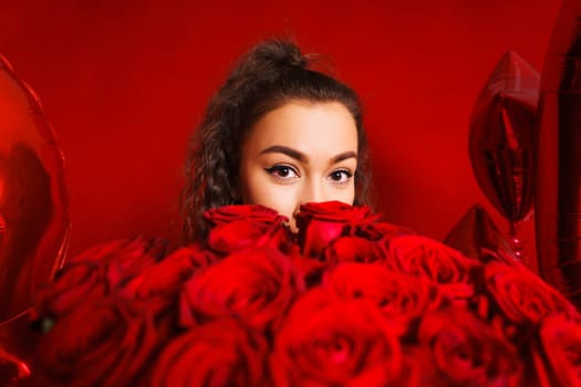Portrait of girl peeking out from behind bouquet of flowers on red background. Portrait of girl peeks out from behind bouquet of flowers on red background. Young woman holding large bouquet red roses