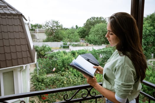 Young caucasian woman stands on the balcony with a notebook in her hand reads records