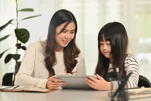 Cute schoolgirl doing homework or learning online with mother at home. Homeschooling, learning and family concept.