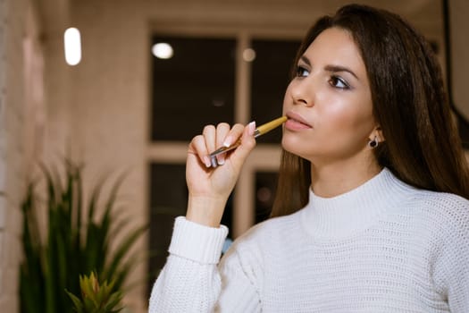 beautiful young woman in a white sweater with a pen in her hand sits pensive at the table