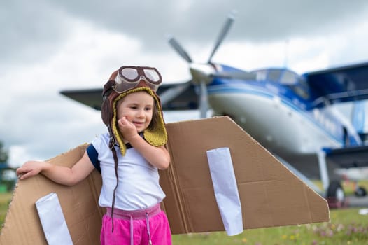 A cute little girl dressed in a cap and glasses of a pilot on the background of an airplane. The child dreams of becoming a pilot