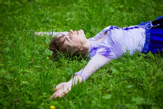 Young woman lies on green grass enjoying the day. Cute Caucasian girl in nature smiles with happiness.