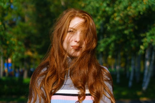 Closeup female portrait of a red-haired Caucasian woman with makeup, with green eyes looking at the camera on a natural background on a sunny day