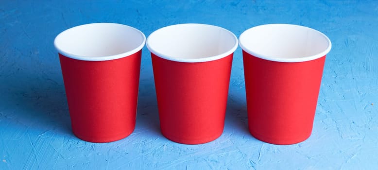 three red paper coffee cups on a blue background with a place to copy the text. Morning concept.