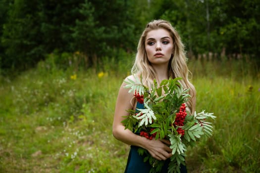 Portrait of a young beautiful blonde woman with a bouquet of rowan berries in nature close-up