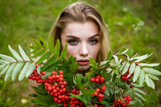 Portrait of a young beautiful blonde woman with a bouquet of rowan berries in nature close-up