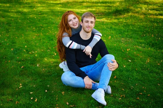 Happy young couple of Caucasian ethnicity man and woman in casual clothes sitting embracing in the park on green grass on a sunny day. Happy relationship between prana and a girl in nature