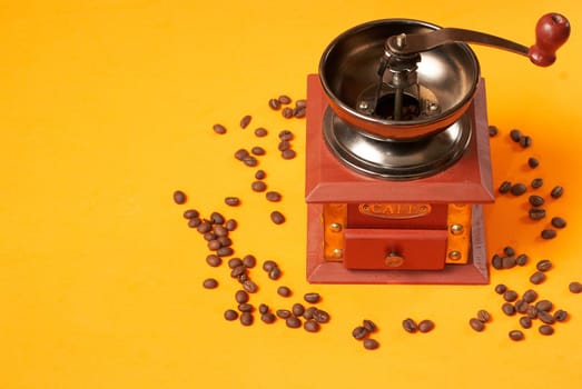 Manual coffee grinder for grinding coffee beans. On an orange background with coffee beans