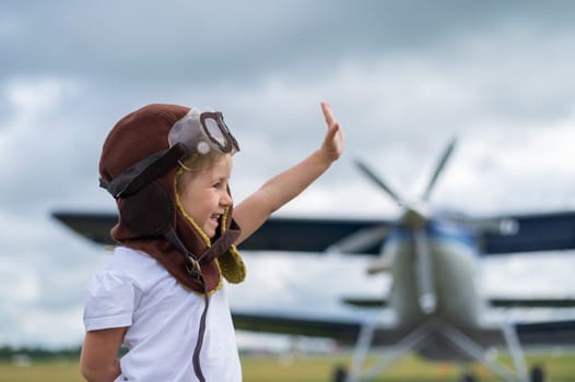 A cute little girl dressed in a cap and glasses of a pilot on the background of an airplane. The child dreams of becoming a pilot