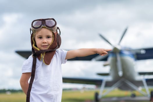 A cute little girl dressed in a cap and glasses of a pilot on the background of an airplane. The child dreams of becoming a pilot