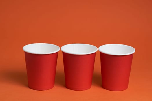 three red paper coffee cups on a brown background with a place to copy the text. Morning concept.