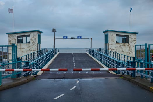 the access to the ferry over the water closed with barriers during the golden rainy day with the horizon and the sea in the background