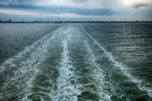 the flowing water seen from the deck of a cruise ship with Den Helder in the background