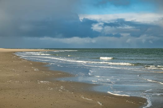 the beach of the island of Texel with dark clouds in the background and small waves in the surf