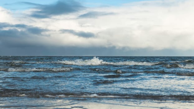 the sea with waves in the surf with the horizon and a cloudy sky in the background