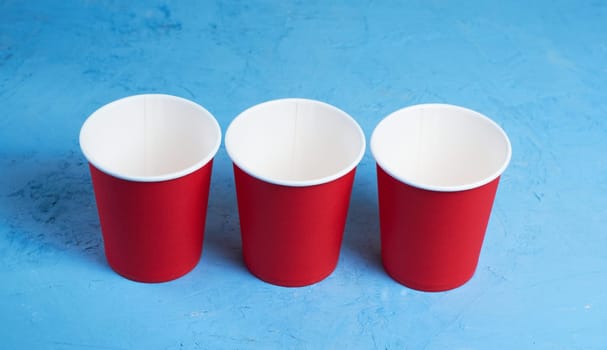 three red paper coffee cups on a blue background with a place to copy the text. Morning concept.