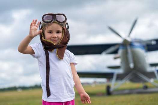 A cute little girl dressed in a cap and glasses of a pilot on the background of an airplane. The child dreams of becoming a pilot