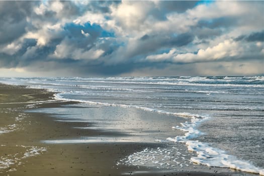 the beach of the island of Texel with dark clouds in the background and small waves in the surf