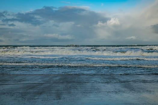 white waves from the sea come from the surf on the beach with a cloudy sky in the background