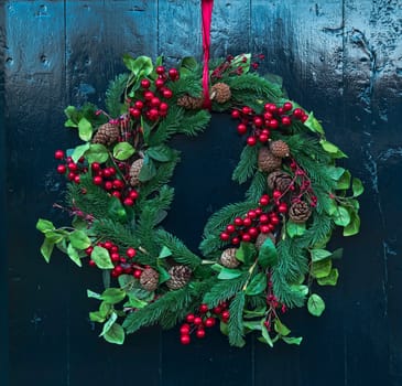 Christmas wreath of fir branches with pine cones and red berries as a decoration on a door