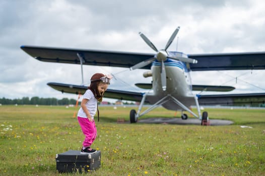 A cute little girl playing on the field by a four-seater private jet dreaming of becoming a pilot.