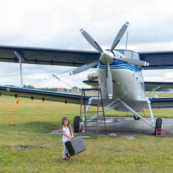 A cute little girl playing on the field by private jet dreaming of becoming a pilot.