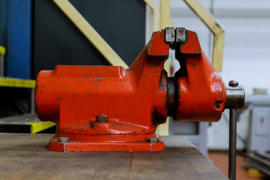 The vise is fixed on the metalworking workbench. Red vise on a wooden table. Bench tools.