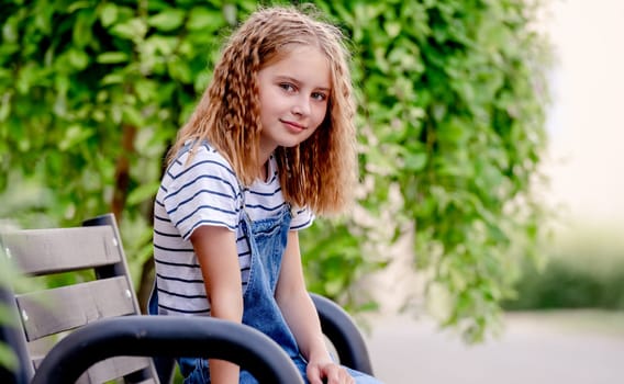 Beautiful preteen girl in city in summertime closeup portrait. Pretty female kid looking at camera in sunny day with blurred background