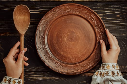 Ukrainian woman sitting in national restaurant and waiting for order. Wooden table, waiting for dish. Empty clay plate with spoon. High quality photo