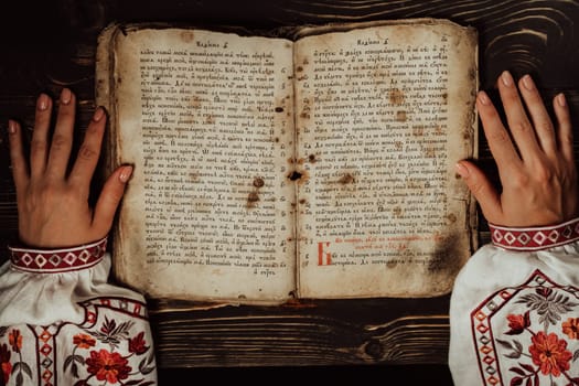 March 2023 - Kyiv, Ukraine. Ukrainian woman reading ancient book - Bible. Concentrated follows finger on paper page under candle light. History of Kyiv Rus. Psalter, 19th century, prayers and psalms.