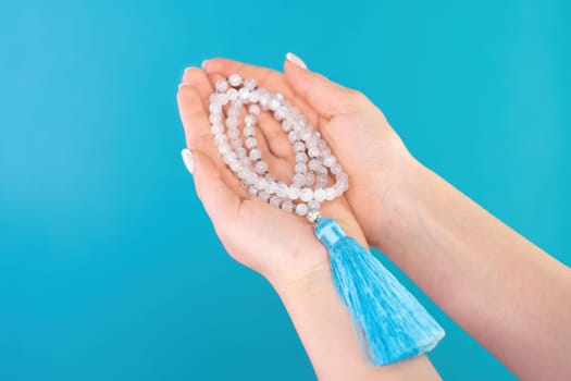 Moon stone mala beads in female hand on blue background. Gemstone strand used for keeping count during mantra meditations. Spirituality, religion, God concept.
