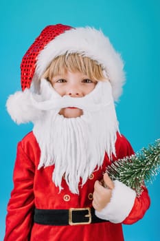 Friendly little Christmas boy in Santa Claus costume on blue background. Happy emotional child with artificial beard. High quality photo