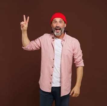 Positive European caucasian man handsome shows gesture of V victory. Cheerful man with silver beard raises his hand with two fingers V shape, indicating gesture of victory, with smile on face. High quality photo
