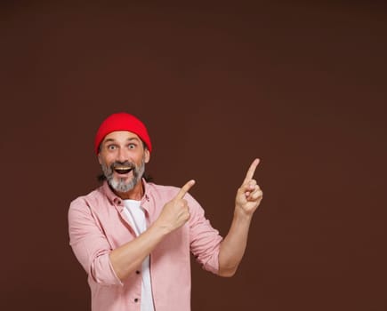 Amazing reaction. a mature European caucasian man points with both hands to the side with copy space isolated on brown. Product placement concept. High quality photo