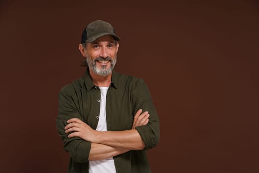 Happy Smiling man. A fisherman in a baseball cap and green shirt stands cross-legged against a brown background with copy space. High quality photo