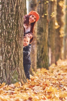 Hiding behind tree. Mother with her little son and daughter is having fun in the autumn park.