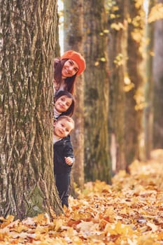 Hiding behind tree. Mother with her little son and daughter is having fun in the autumn park.