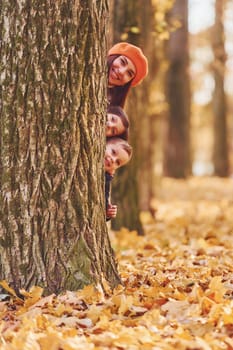 Hiding behind tree. Mother with her little son and daughter is having fun in the autumn park.