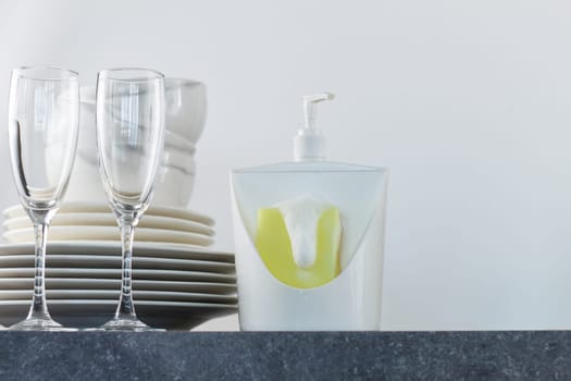 Clean dishes with dishwashing gel and yellow sponges on the kitchen table.