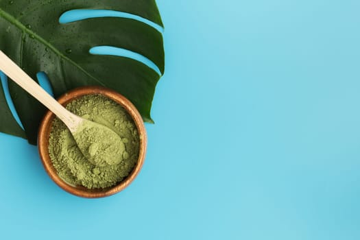 Wooden spoon with matcha tea in a wooden plate and monstera leaf on a blue background. Matcha green tea powder. copy space