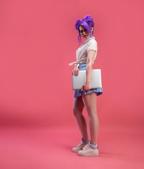 sexy girl with glasses with purple hair with a laptop in summer clothes on a pink background copy paste