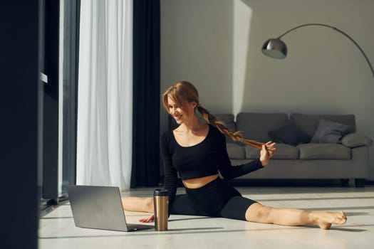 Using laptop. Woman in sportive clothes doing yoga indoors.