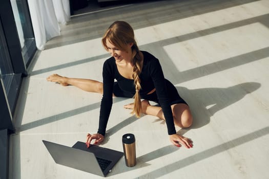 Using laptop. Woman in sportive clothes doing yoga indoors.