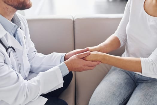 Holding customer by the hands. Professional medic in white coat is in the clinic.