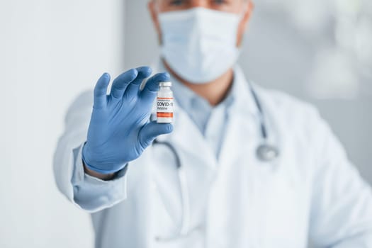 Holding test tube with COVID-19 vaccine. Professional medic in white coat is in the clinic.