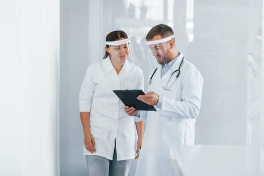 In protective masks. Two doctors in white coats is in the clinic working together.