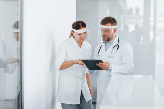 In protective masks. Two doctors in white coats is in the clinic working together.