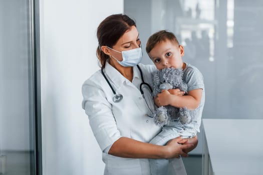 With little kid in hands. Professional medic in white coat is in the clinic.
